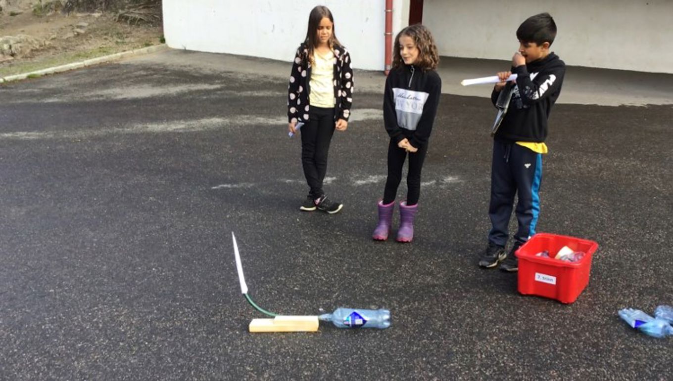 Foto: Ridwan Aouragh 3 elever står ved siden av en tomflaske med rakett i .