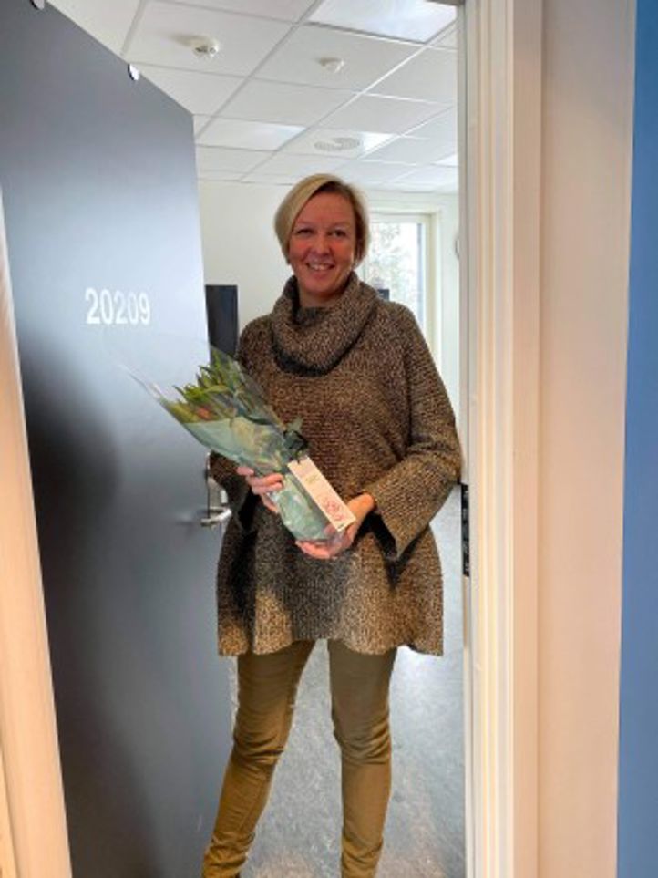 Bilde av Linda Tvedt som nå skal videre til en annen jobb. Hun står i døren med en blomsterbukett i hendene.