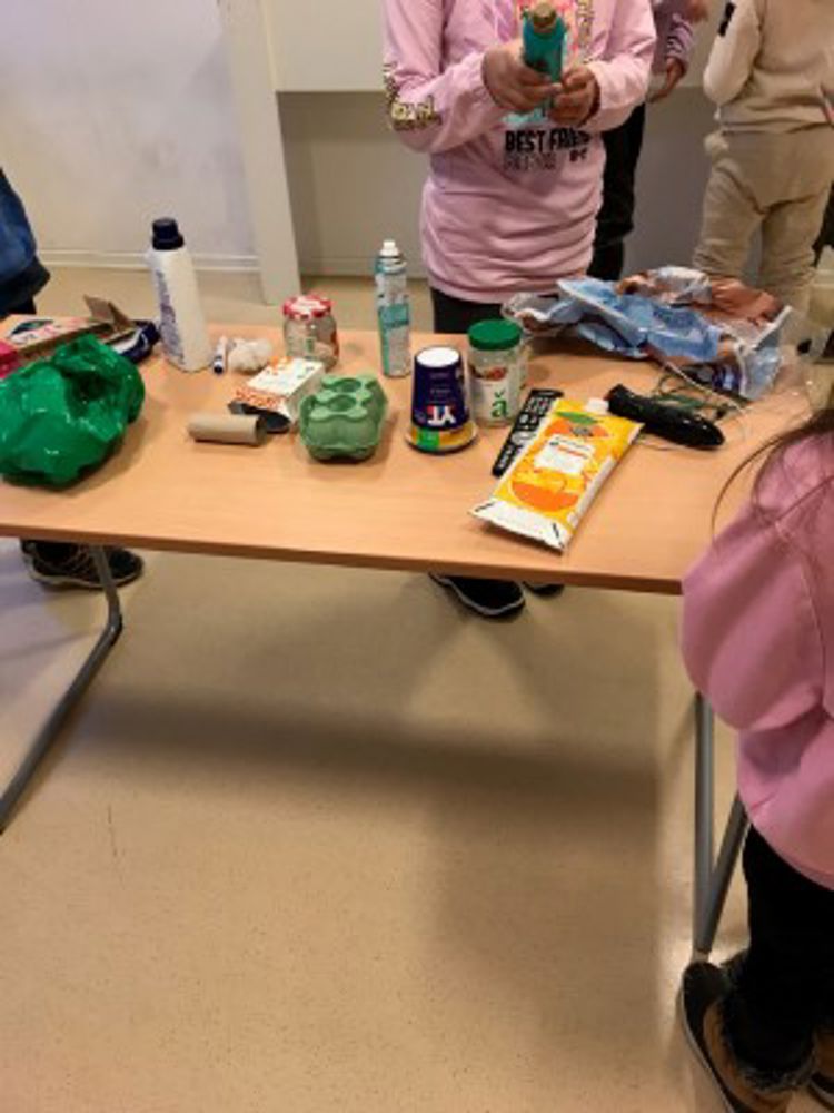Elevene står ved et bord med ulike ting på bordet, og får kunnskap om hvordan de skal avfallssortere det.
