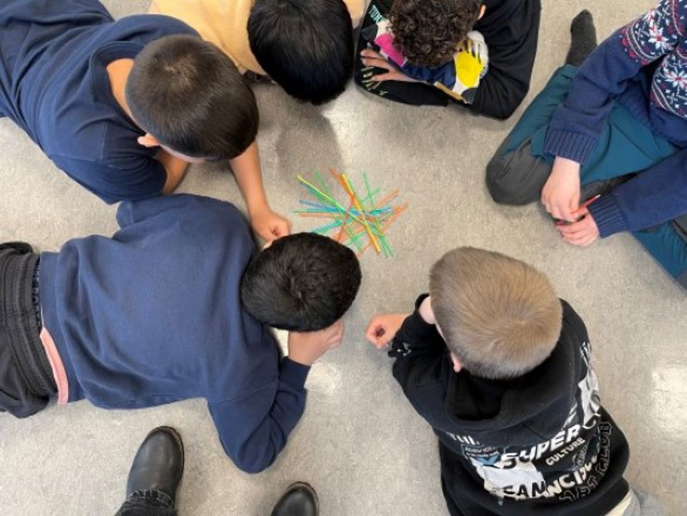 Guttene ligger på gulvet på magen i ring og spiller pinnespillet Mikado